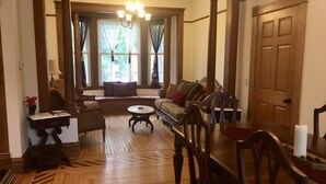 A traditional interior with a wooden floor, a sofa set, a dining table with chairs, a chandelier, and a large wooden door. - Historic 1880s Home (Osceola)