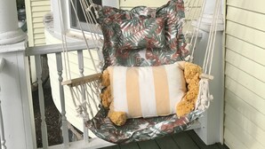 A hammock chair with a striped cushion and a pillow, suspended by ropes and a wooden beam, attached to a white railing on a porch. - Historic 1880s Home (Osceola)