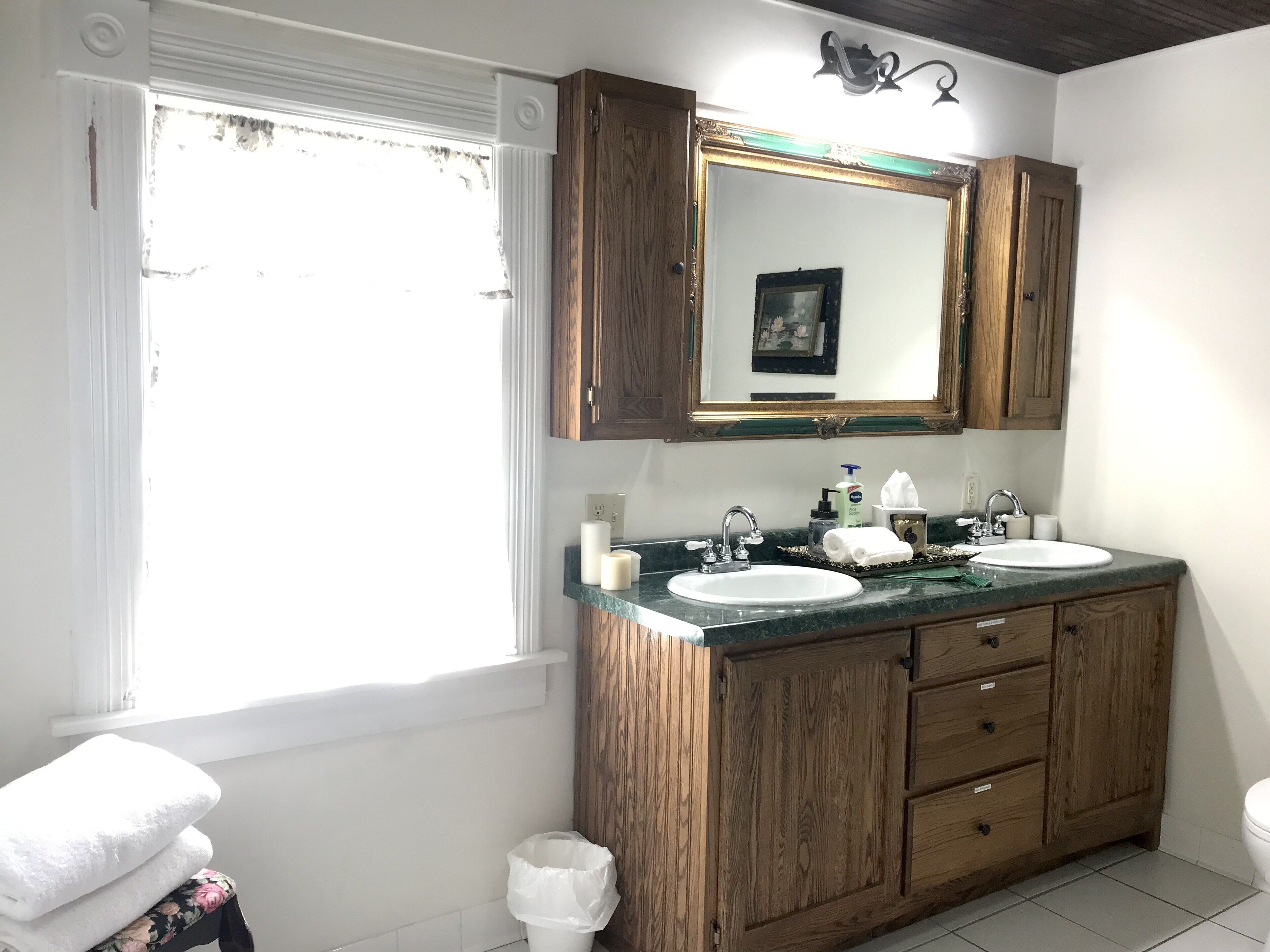 A bathroom with wooden cabinets, a double sink, a mirror, and a window.