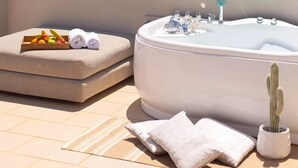 A spa area with a hot tub, a cushioned seating area with towels, a tray of fruits, and a cactus plant. - Skiathos Avaton Hotel (Skiathos)