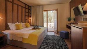 A bedroom with a bed, bedside tables, a TV, a desk, and a view of the outdoors. - Skiathos Avaton Hotel (Skiathos)