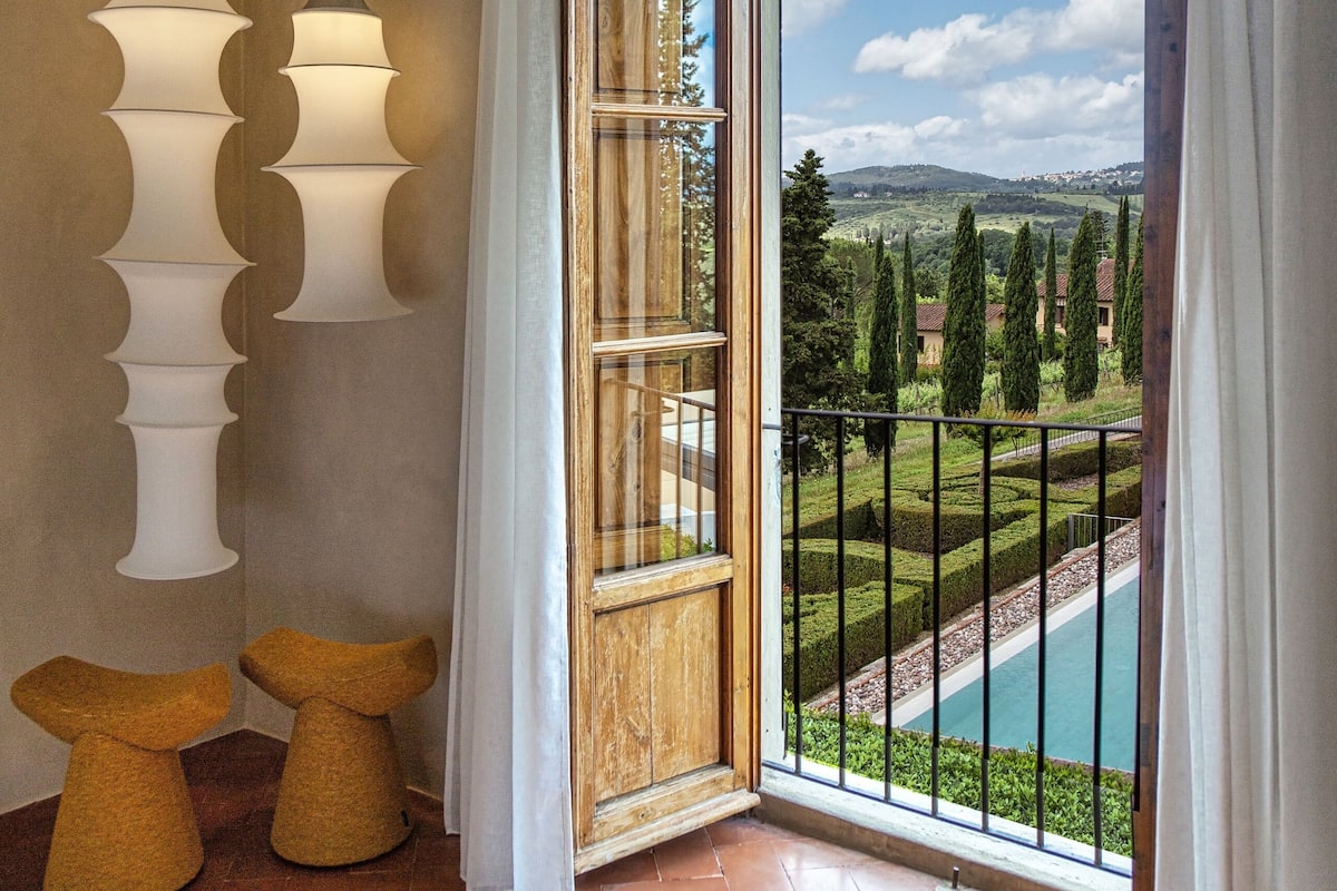 A room with a large window, a view of a pool, and two hanging lamps.