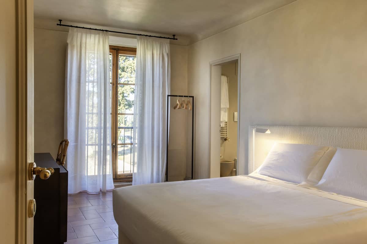 A hotel room with a bed, a desk, and a window with curtains.