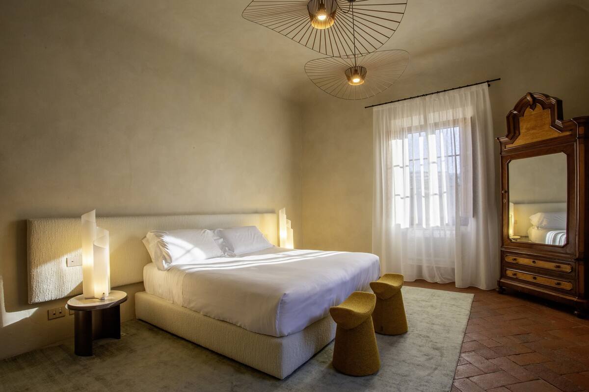 A bedroom with a large bed, bedside lamps, a wooden dresser, and a window with curtains.