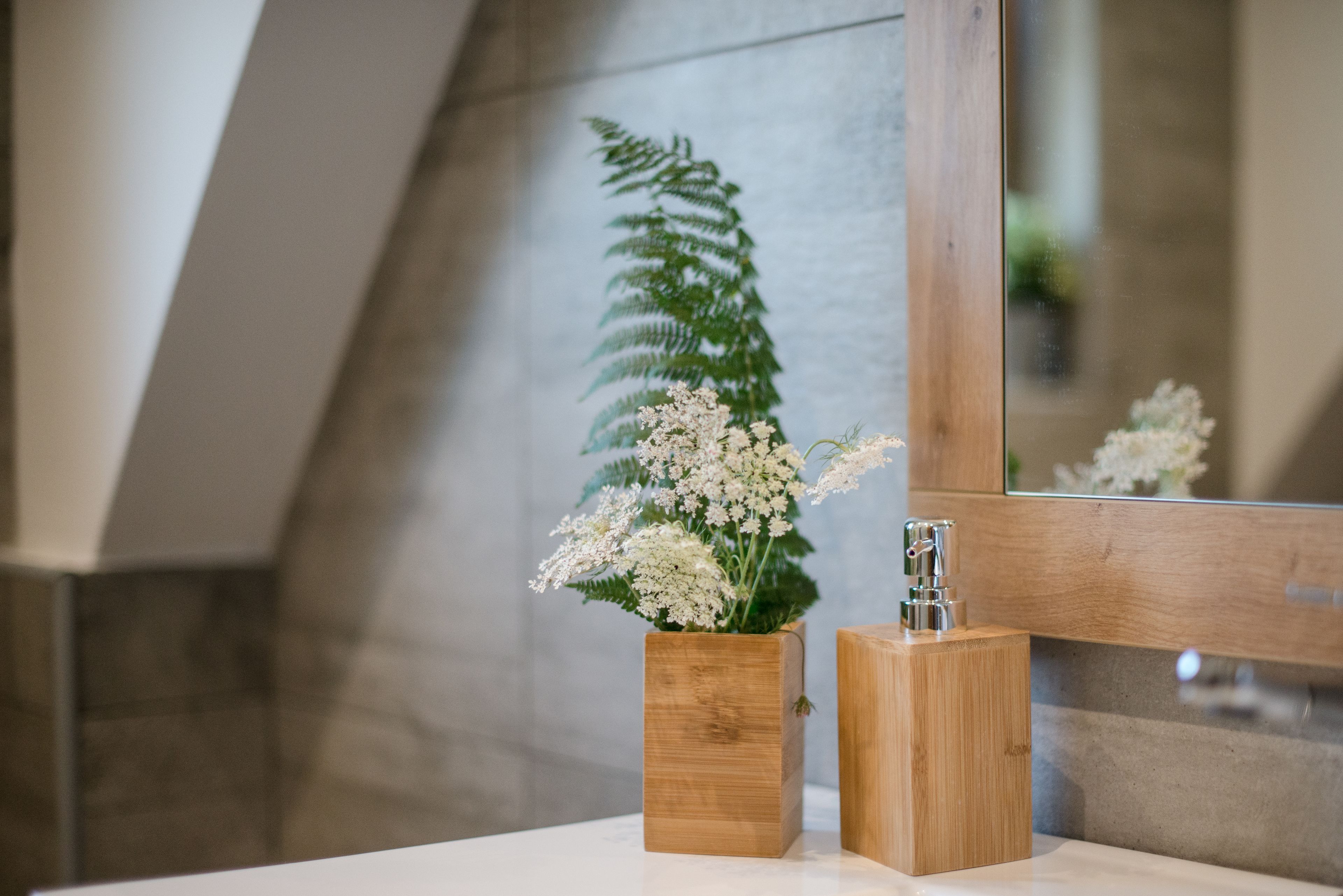 A bathroom with a wooden vanity, a mirror, and a potted plant with white flowers.