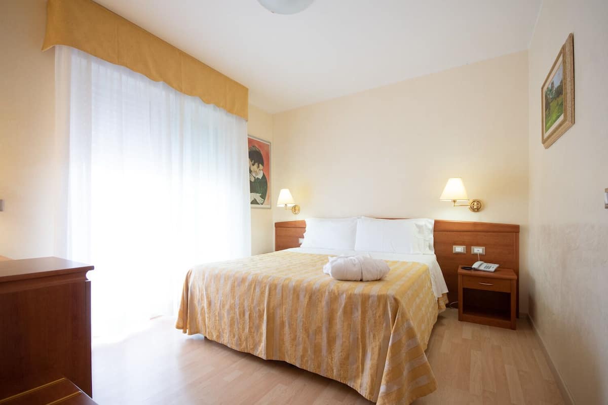 Een hotelkamer met een bed, nachtlampjes, een nachtkastje, een houten dressoir en een schilderij aan de muur.