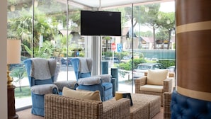 A modern lounge area with wicker furniture, a large TV screen, and a view of the street outside. - Hotel Arizona (Lignano Sabbiadoro)