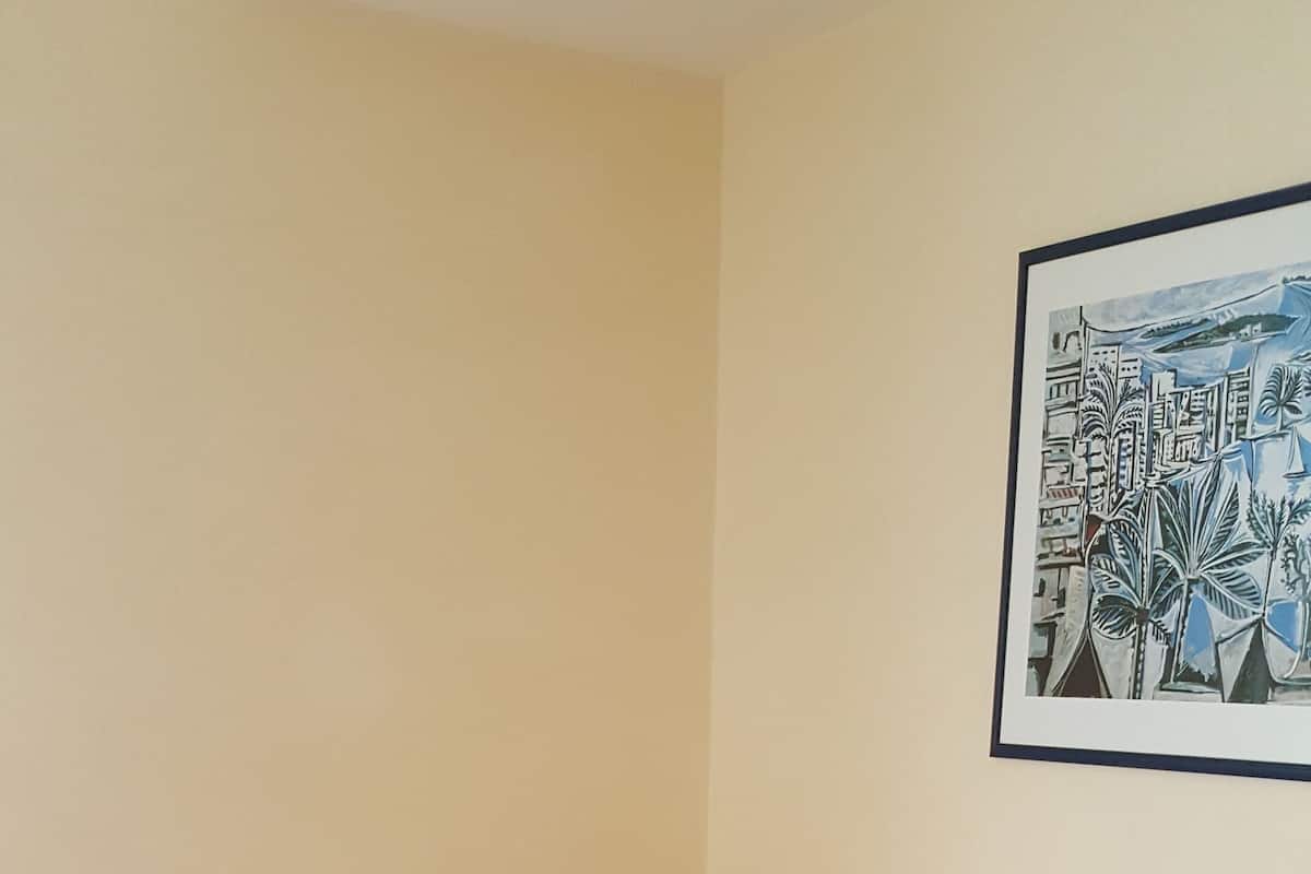Een hotelkamer met een eenpersoonsbed, een nachtkastje, een rood tapijt en een ingelijste foto aan de muur.