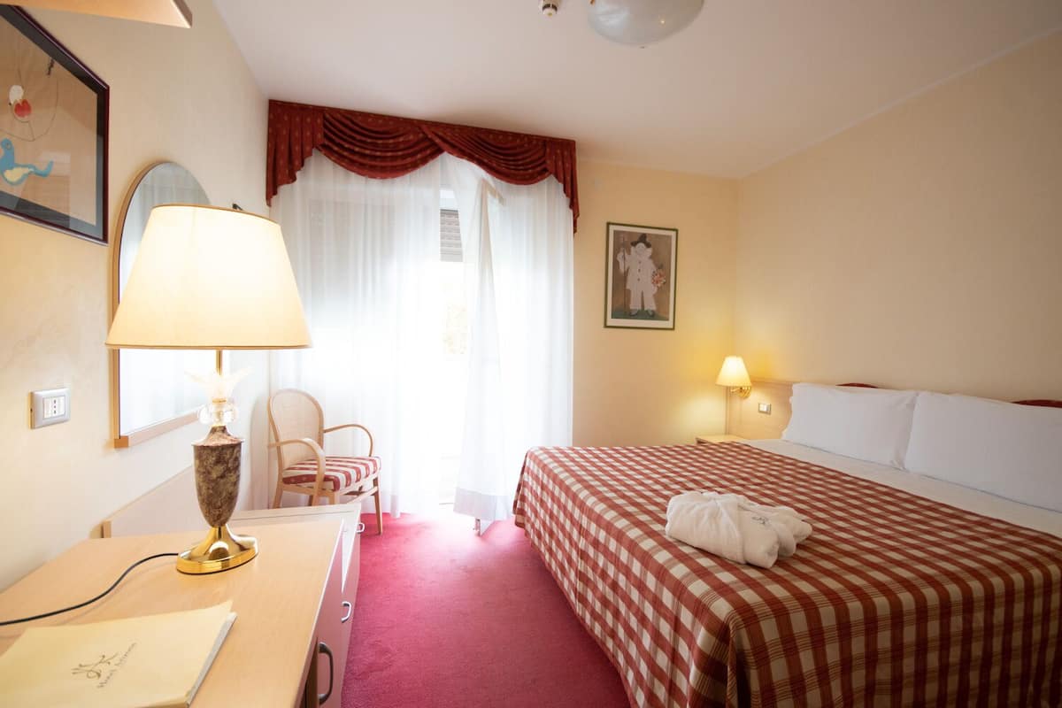 Een hotelkamer met een geruit beddegoed, een bureau met lamp, een stoel en een schilderij aan de muur.
