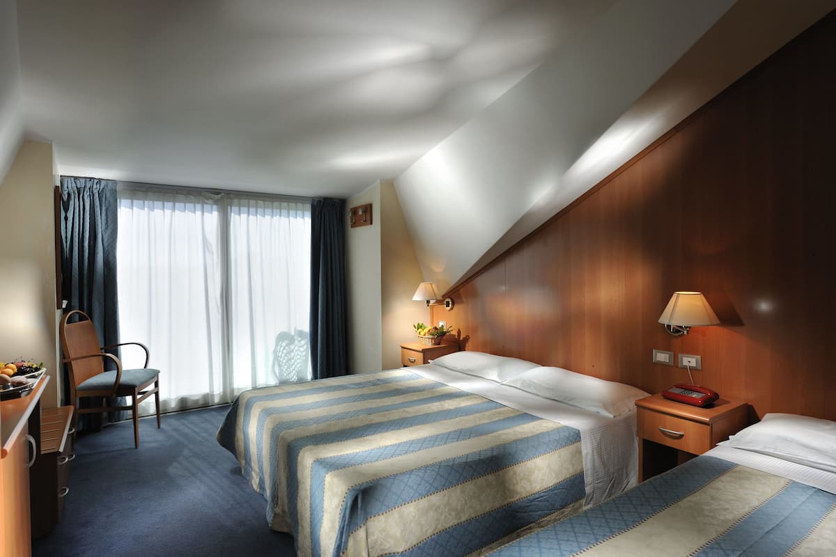 Een hotelkamer met twee bedden, een bureau, een stoel en een raam met gordijnen.