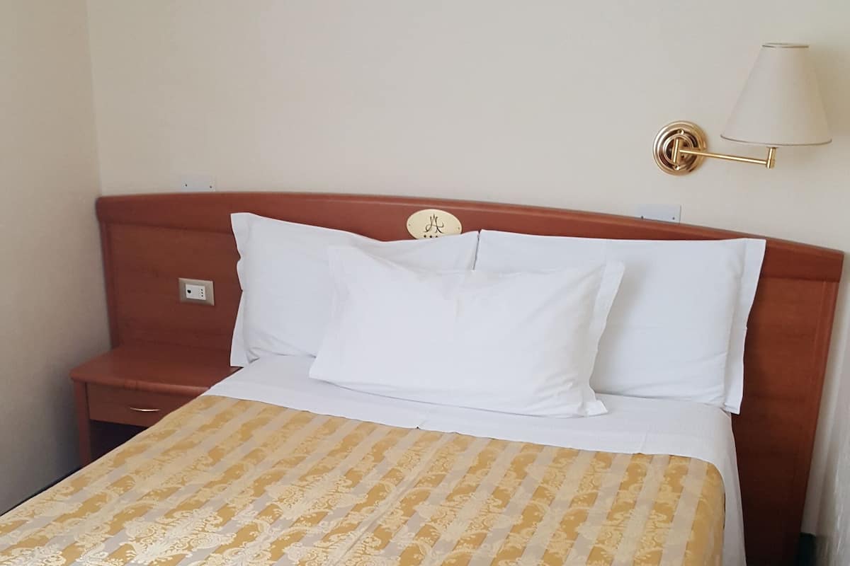 Een hotelkamer met een bed, nachtkastje, lamp en een stopcontact.