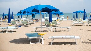 A beach with rows of sun loungers and blue umbrellas. - Hotel Arizona (Lignano Sabbiadoro)