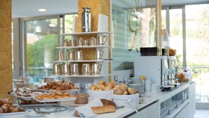 A buffet with various pastries and bread, a coffee station, and a view of greenery outside. - Hotel Arizona (Lignano Sabbiadoro)