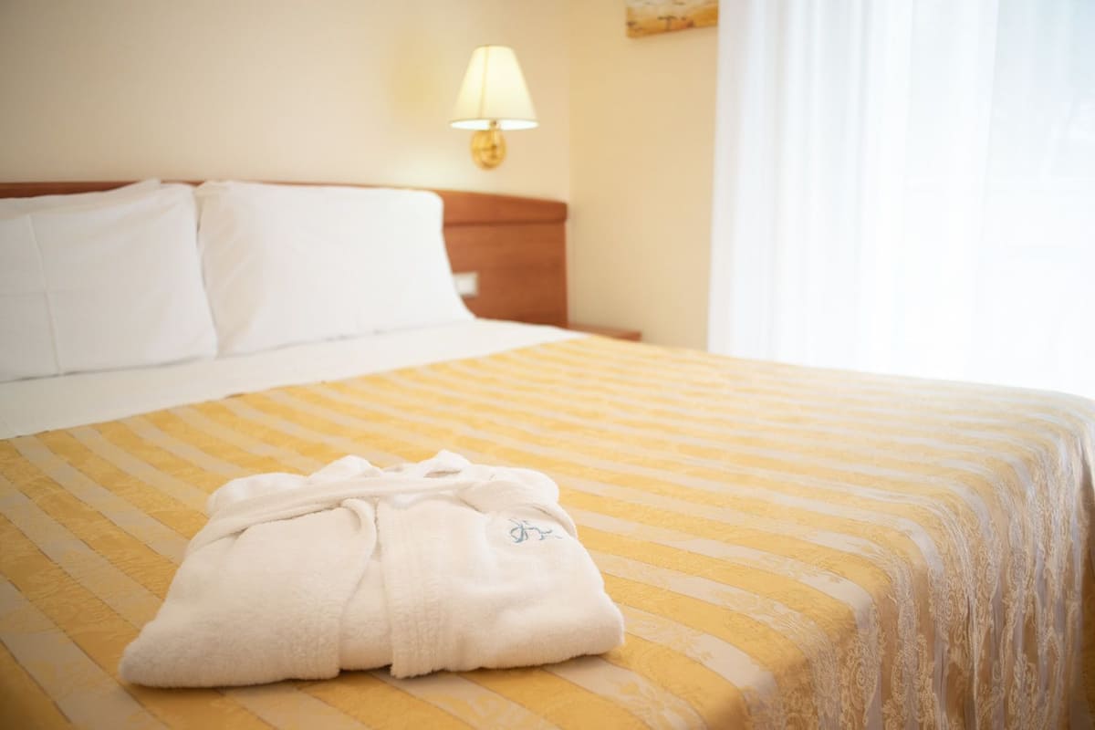 Een net opgemaakt bed met een gestreept geel-wit dekbed, een wit kussen en een witte badjas op het bed.