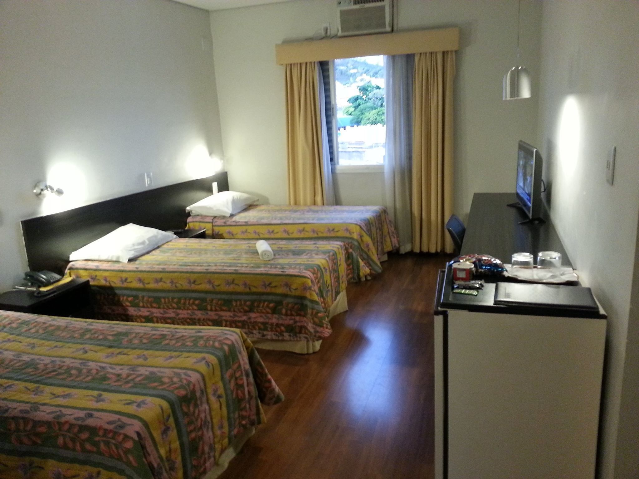 Ein Hotelzimmer mit zwei Betten, einem Schreibtisch, einem Stuhl, einem Fernseher und einem Fenster mit Vorhängen.