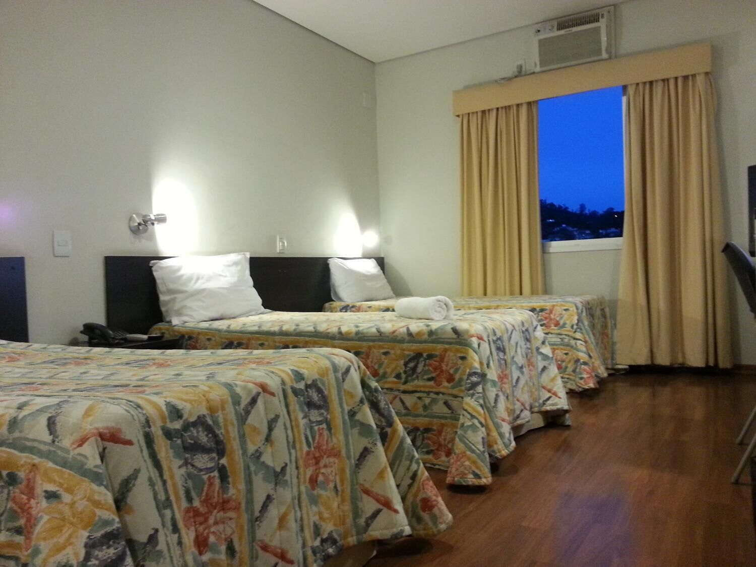 A hotel room with two beds, a desk, a telephone, and a window with curtains.