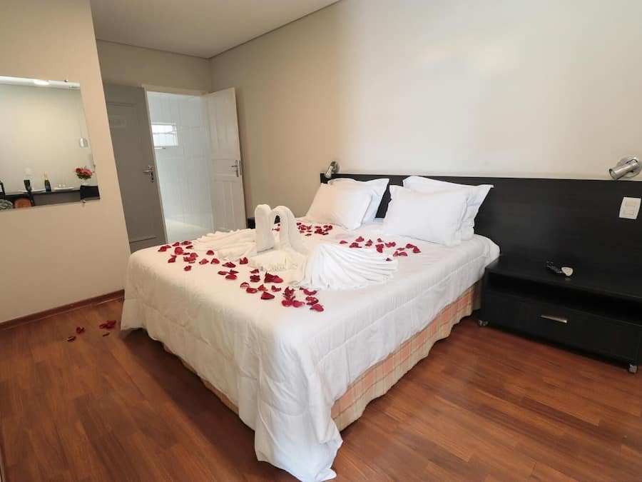 A neatly made bed with white linens and rose petals, a black headboard, and a wooden floor.