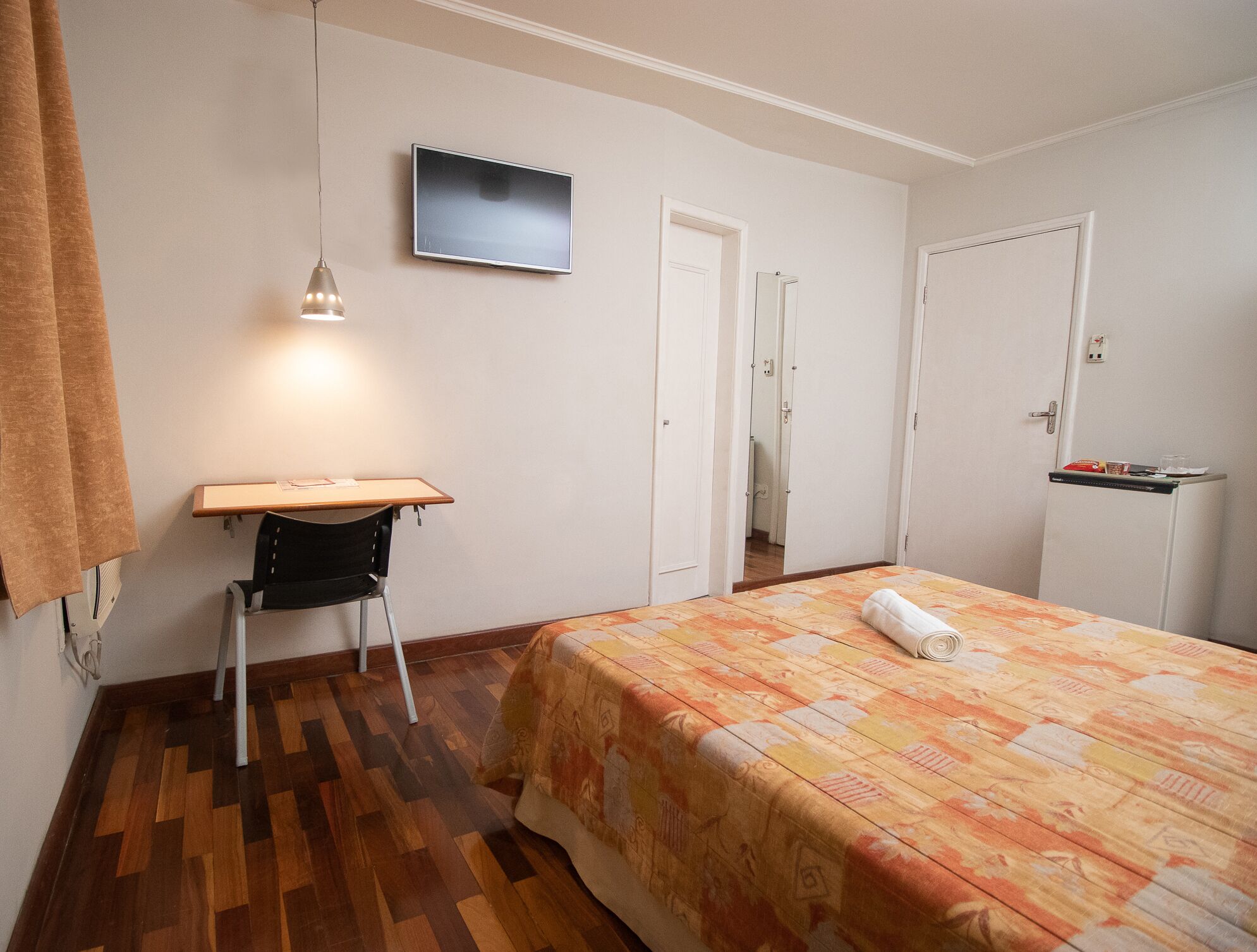 A bedroom with a bed, a desk, a chair, a television, and a wardrobe.