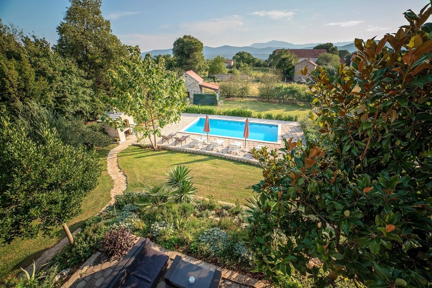 A pool surrounded by a garden with a stone pathway leading to it.