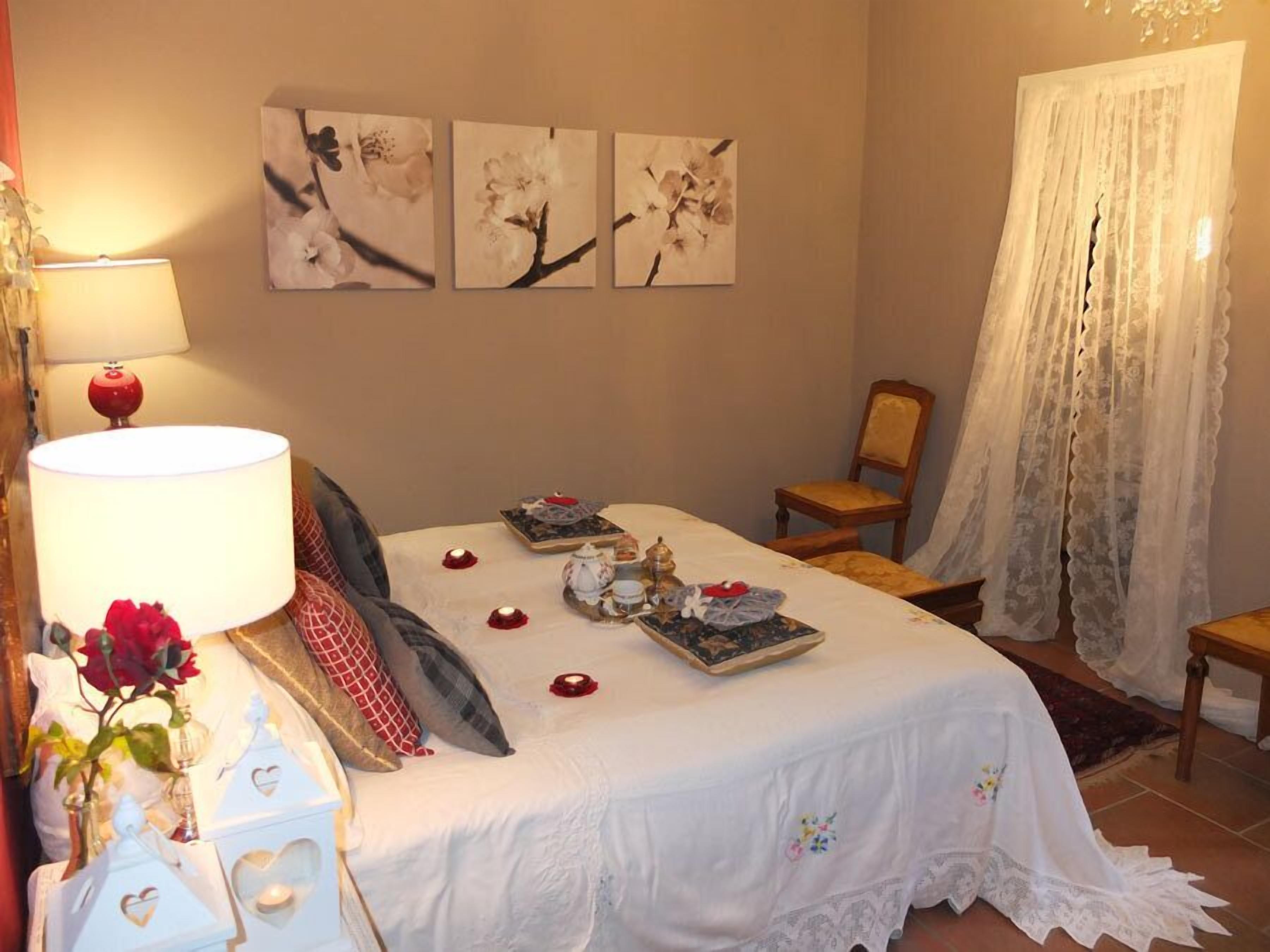 A neatly arranged bedroom with a bed, bedside table, lamp, and floral decorations.