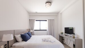 A hotel room with a bed, a desk, a television, and a window with curtains. - Victoria Village (Asunción)