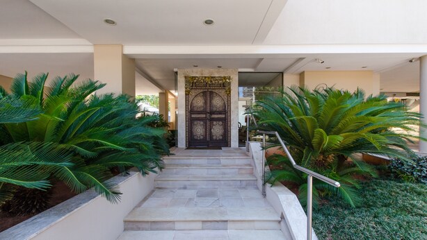 A staircase leading to a door with intricate designs, flanked by lush green plants. - Victoria Village (Asunción)