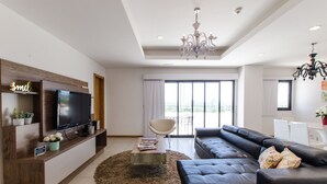 A modern living room with a flat-screen TV, a sofa, a coffee table, and a large window offering a city view. - Victoria Village (Asunción)
