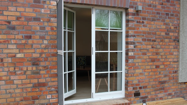 A brick wall with a white-framed window and a small step leading to a wooden deck. - Ferienwohnung Remise (Lübbenau/Spreewald)