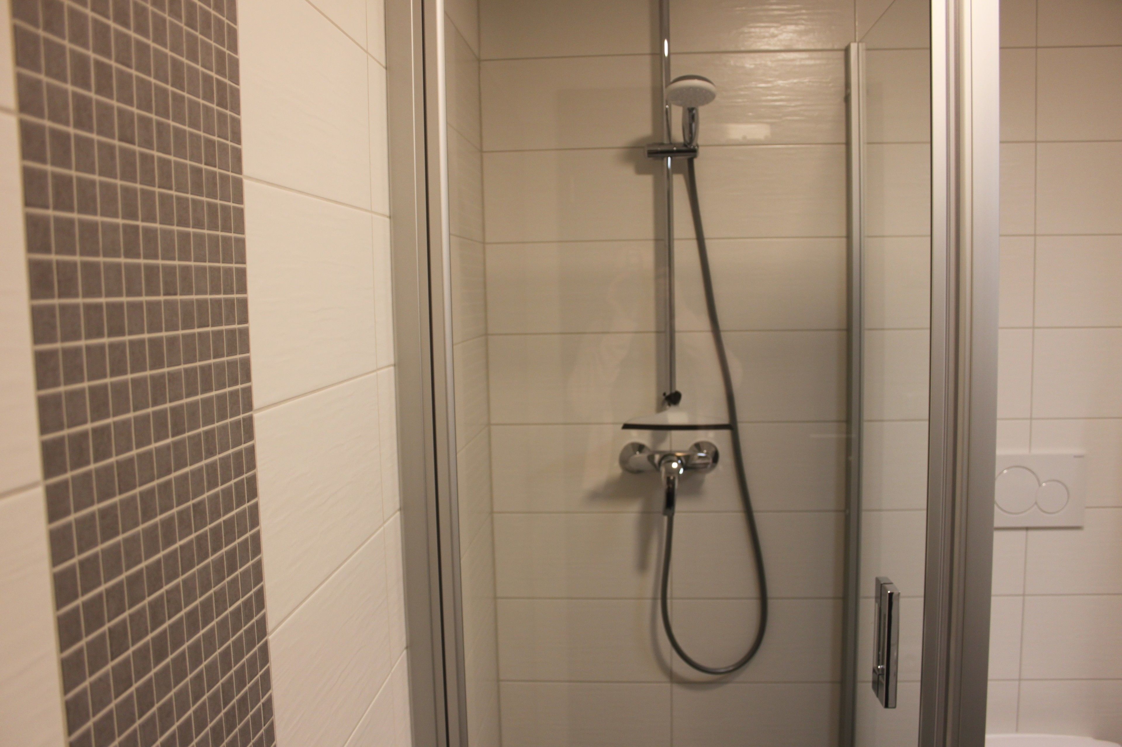 A glass-enclosed shower with a handheld showerhead and a wall-mounted faucet.
