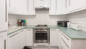 A compact kitchen with white cabinets, a stainless steel stove, and a microwave. - Keysan House 1 (London)