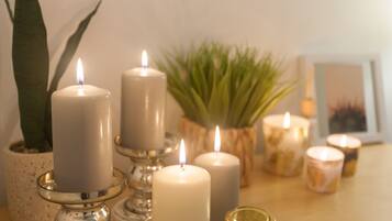 A table with several white candles on stands, a potted plant, and a framed picture.