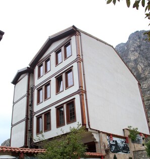 Ein mehrstöckiges Gebäude mit weißer Fassade und braunen Akzenten, mit zahlreichen Fenstern und einem Bergpanorama im Hintergrund.