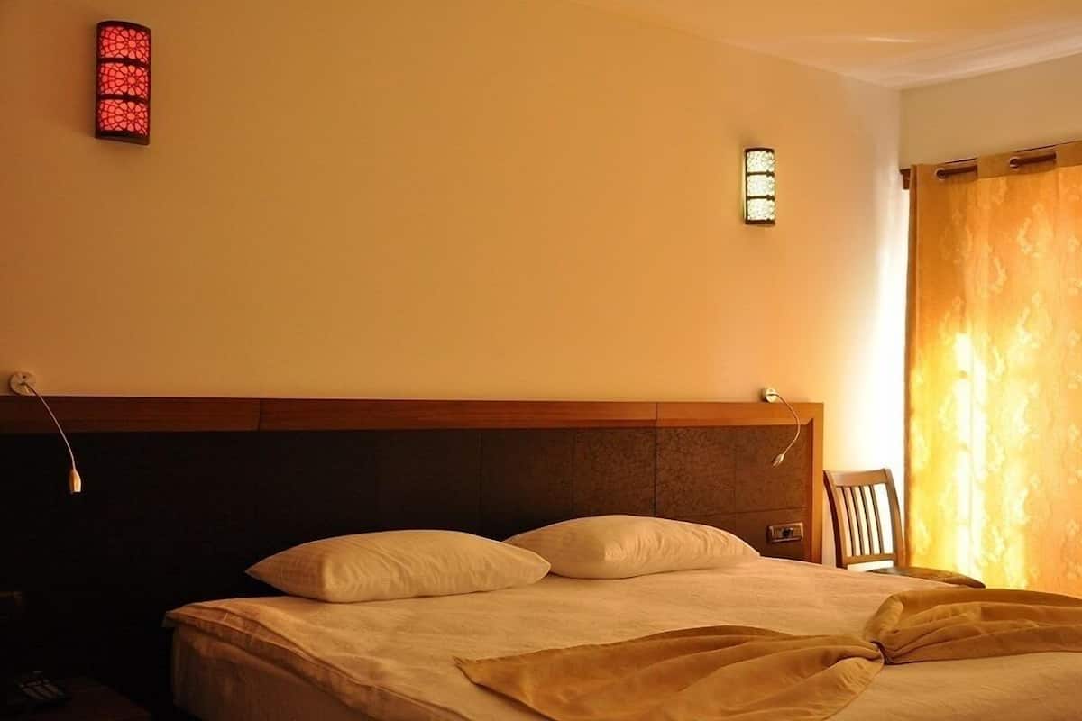 A hotel room with a bed, a nightstand, a wall-mounted lamp, and a window with curtains.