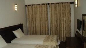 A hotel room with two beds, a desk, and a mirror.