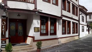 A multi-story hotel with a white facade and brown trim. It features a balcony with wooden railings and a set of double doors with a small porch area.