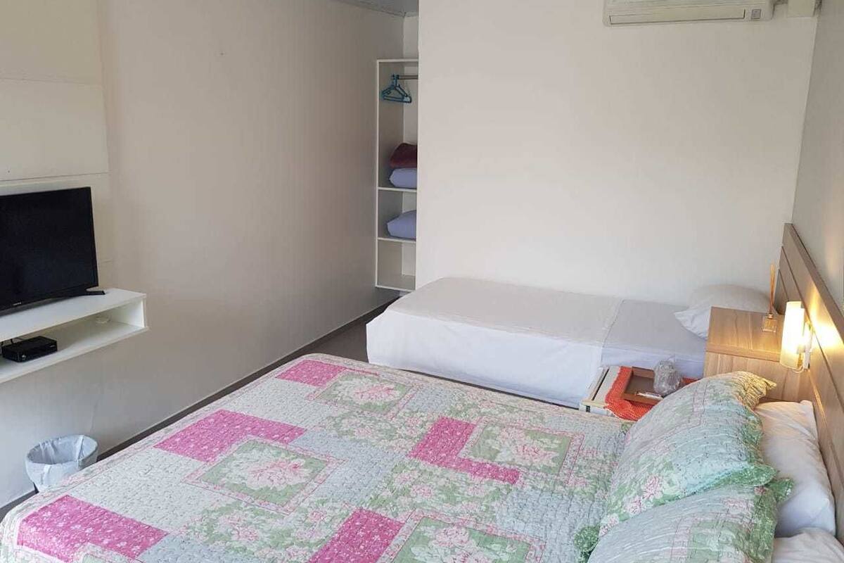 A small, neatly arranged bedroom with a bed, a TV, a shelf, and a bedside table with a lamp.