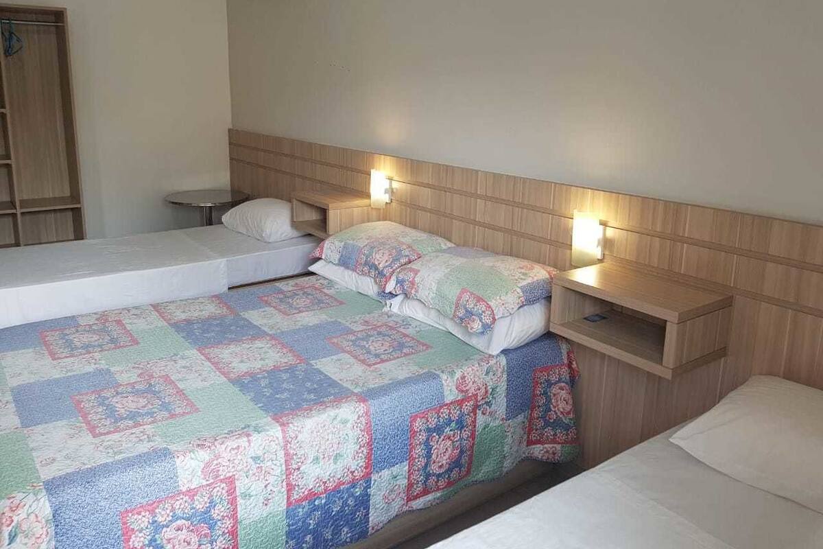 A hotel room with a bed, two bedside tables, and a wall-mounted air conditioner.