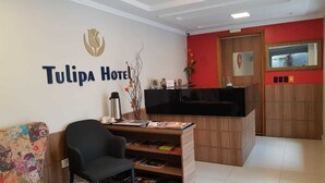 A reception area with a desk, chairs, a TV, and a wall with the hotel name. - Tulipa Hotel (Torres)