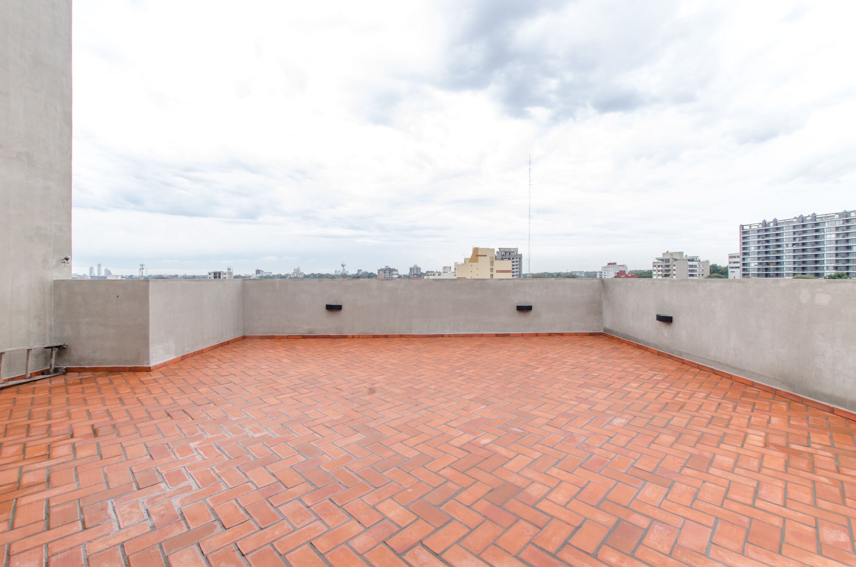 A rooftop terrace with a brick floor and a view of surrounding buildings.
