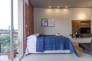 A modern bedroom with a large bed, a TV mounted on the wall, and a balcony with potted plants. - Soho Loft Studio con Estilo en Mercedes (Asunción)