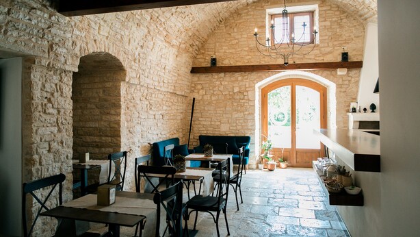 A rustic stone interior with a wooden door, stone walls, and a chandelier. Tables and chairs are arranged for dining. - San Marco Antico Relais (Bitonto)