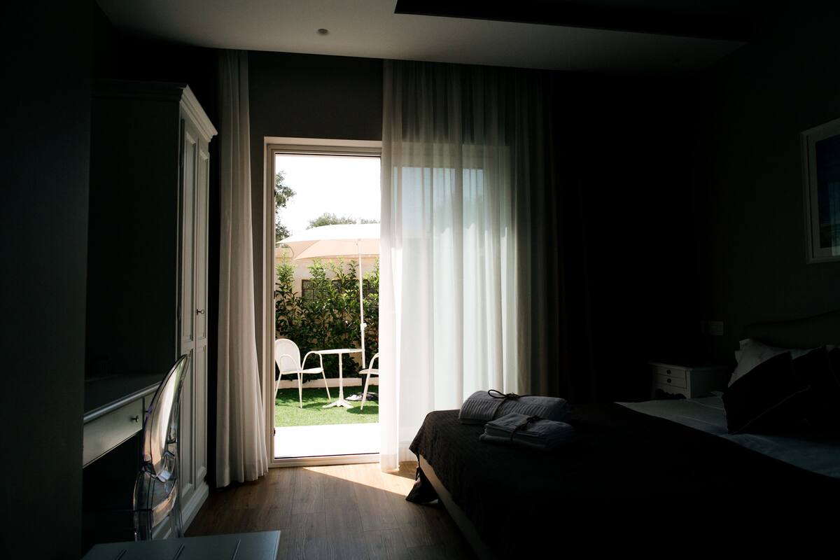 A hotel room with a bed, a desk, and a view of an outdoor area with a table and chairs.