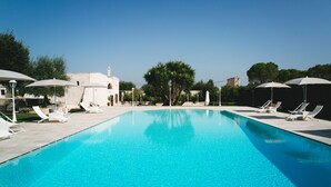 A clear blue swimming pool with lounge chairs and umbrellas, surrounded by trees and a stone building. - San Marco Antico Relais (Bitonto)