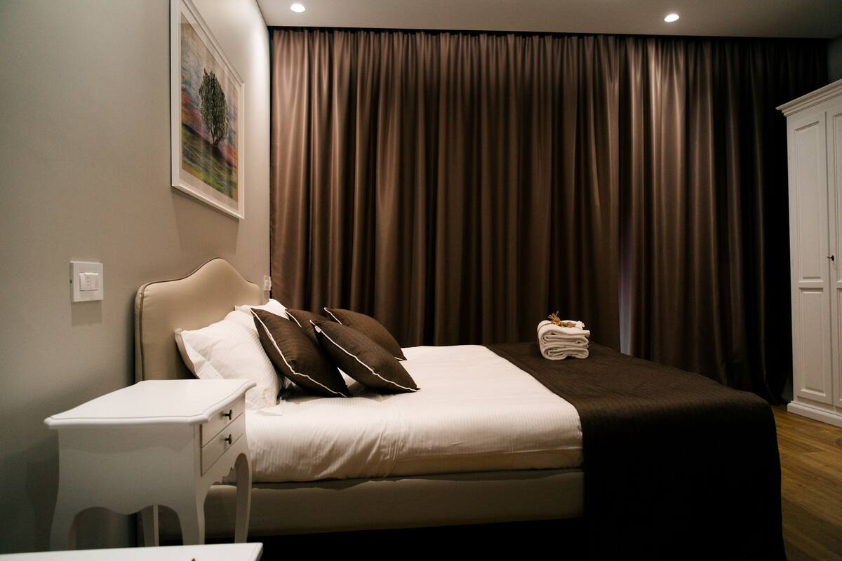 A hotel room with a bed, a nightstand, a painting on the wall, and a wardrobe.
