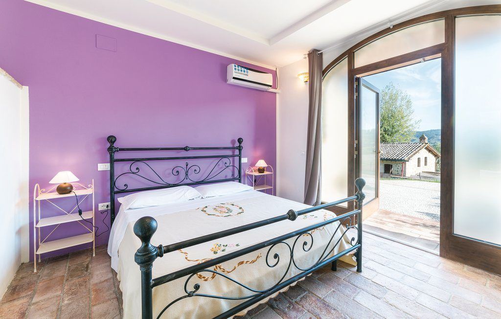 A room with a bed, purple walls, an air conditioning unit, a lamp, and a view through a glass door.