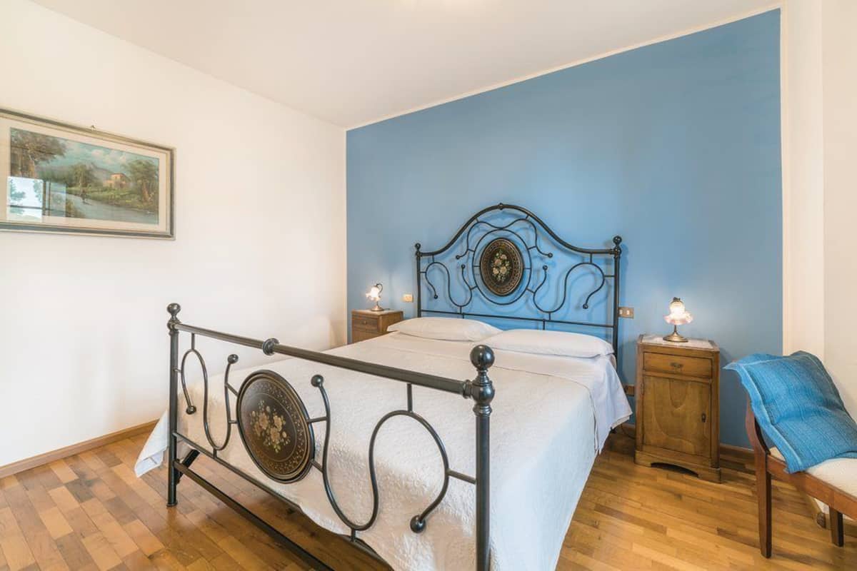 Une chambre à coucher avec un lit en métal, un mur d’accent bleu, une table de chevet avec une lampe et une chaise.