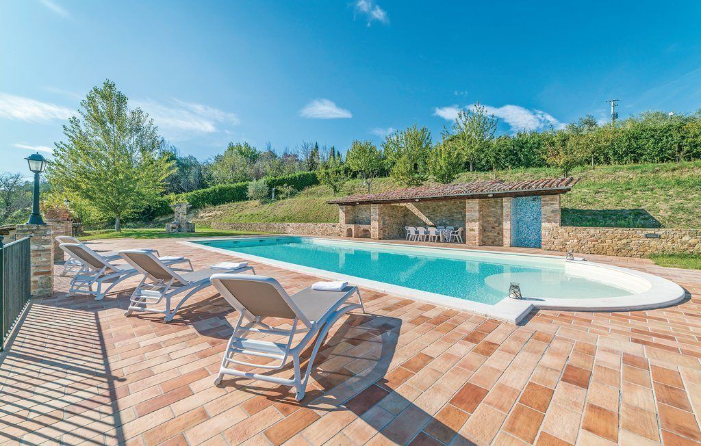 A swimming pool with lounge chairs, a stone structure, and a view of trees and hills.
