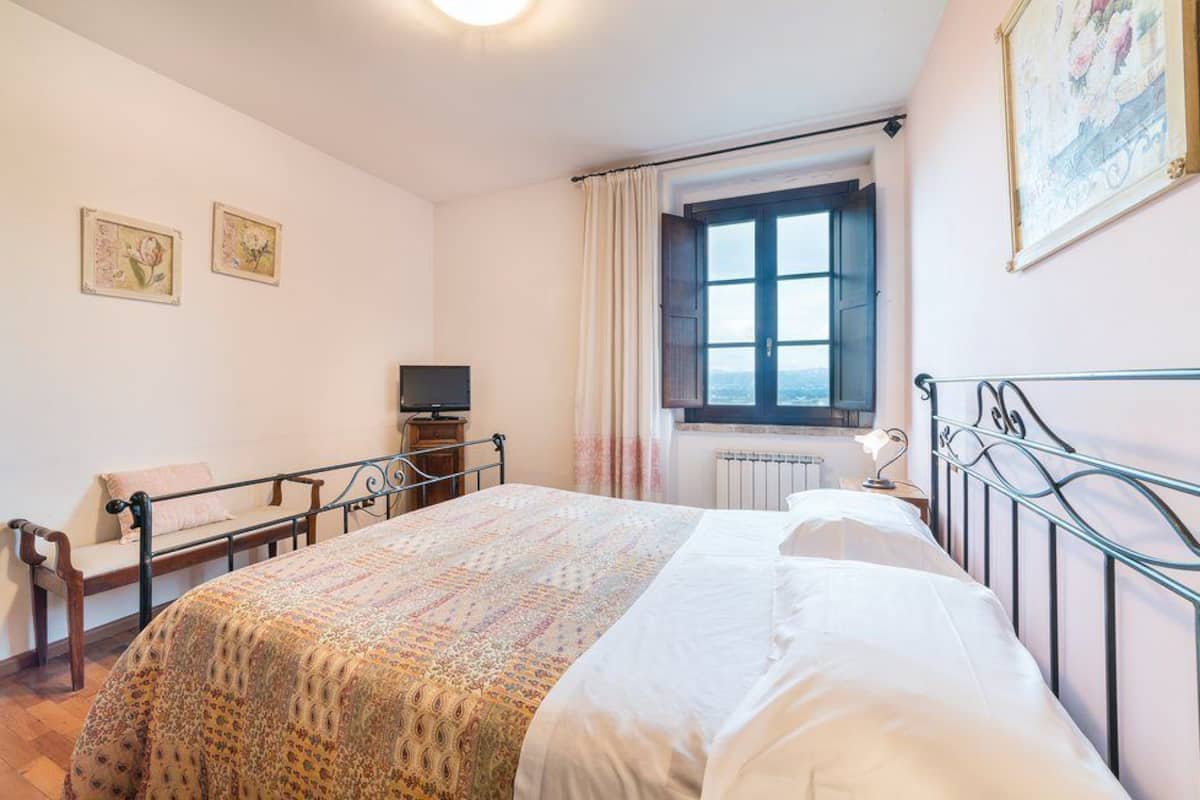 Une chambre à coucher avec un lit, une télévision, une fenêtre avec des rideaux et deux tableaux encadrés accrochés au mur.