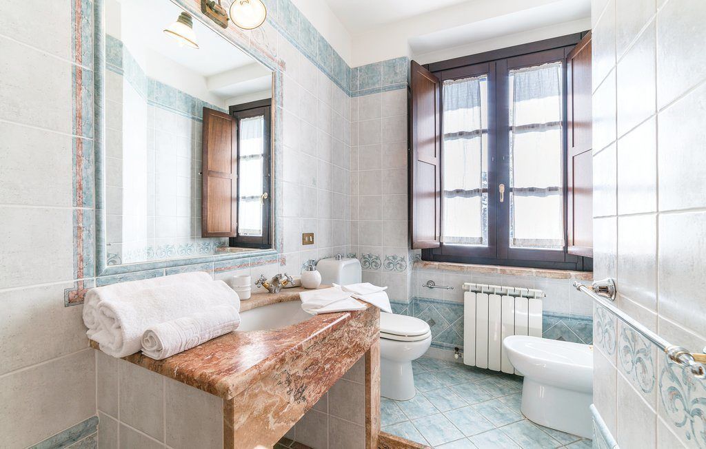 Une salle de bain avec un lavabo en marbre, deux toilettes, une fenêtre et un radiateur.