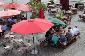 An outdoor café with tables and chairs under red and green umbrellas, surrounded by brick flooring. - Ferienwohnung Zeitreise (Lübbenau/Spreewald)